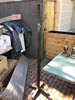 Full view of the vintage wooden coatrack standing on red brick floor next to other outdoor items.