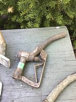 Single metal gas pump nozzle with rust and wear, displayed on wood surface with greenery background.