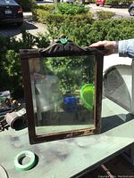 Wood framed mirror with carved crest on top shown outdoors on a green surface with some surrounding items.