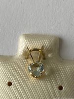 Front view of heart-shaped aquamarine pendant set in 14K yellow gold on a fabric display card.