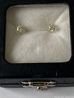 Photo of two round cubic zirconia stud earrings in yellow gold setting, displayed on white cushioned insert inside black box with transparent lid.