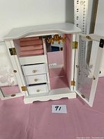 Open front view of the white wooden jewelry cupboard showing the interior with mirror, drawers, padded ring holders, and hooks