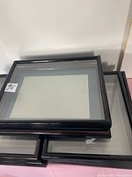 Stack of black picture frames with glass fronts on table surface.