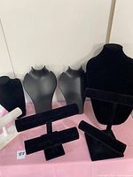 Photo showing an assortment of jewelry display stands including black bust-style necklace holders, black horizontal bars, a small black round stand, and a white horizontal bar stand marked Holiday.