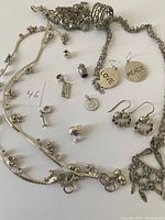 Photo of vintage silver and sterling silver jewelry pieces arranged on light surface. Includes necklaces, charms, and earrings.