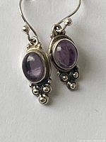 Close-up of one sterling silver earring with oval cabochon amethyst stone and silver bead accent