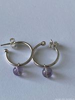 Pair of sterling silver hoop earrings with amethyst bead dangles shown on a white background, displaying front and side views.