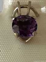 Close-up view of round faceted purple amethyst set in prong sterling silver pendant.