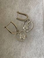 Pair of sterling silver dangle earrings with heart-shaped CZ stone design, shown on white textured background.