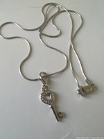 Full view of the sterling silver necklace laid flat showing the key pendant and chain clasp.