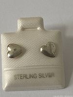 Front view of two sterling silver heart shaped stud earrings on a white textured display card stamped with 'STERLING SILVER'.