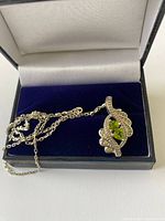 Sterling silver necklace with a leaf-shaped pendant featuring two green peridot stones inside a jewelry box.
