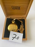 Gold pocket watch with gold chain inside a wooden box labeled 'Swank'