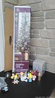 Photo showing boxed new prelit 4-foot Christmas tree, Hallmark Coca Cola music globe package, and assortment of glass ornaments arranged in front