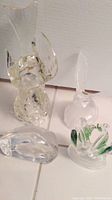 Four glass bird figures: Mats Johansen paperweight with swan engraving, large clear glass bird, smaller glass bird, and green glass swans on a base.