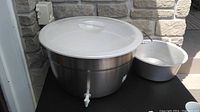 Large insulated stainless steel drink dispenser with plastic lid and white spigot, next to vintage galvanized metal basin
