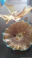 Amber chalet glass bird figurine beside an amber art glass bowl with turquoise rim on reflective surface