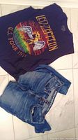 Photo showing sleeveless Led Zeppelin black t-shirt with colorful 1977 US Tour print alongside blue Buffalo jeans size 34/32 with belt loops and pockets.