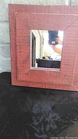 Front view of rustic red square mirror with wooden weathered frame showing mirror and nails securing it.