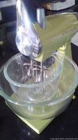 Front and side view of vintage Sunbeam Mixmaster mixer with attached beaters and large glass mixing bowl on base. Shows chrome speed control and pale green colored body.