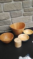 Five kitchen items on black surface with stone background: a large wooden bowl, a Pampered Chef wooden bowl, two small blue bowls, and a wooden canister with lid.