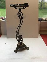 Full view of the brass smoker's stand showing the swan-shaped curved openwork design and triple claw-foot base, missing glass insert on top.