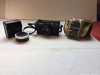 Full front view showing Canon A35F camera, Vivitar teleconverter lens, black case, and worn cream Canon case.