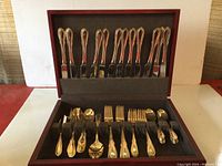 Full set of goldtone flatware arranged inside storage box showing knives, forks, spoons, and serving pieces.