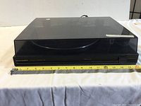 Front view of Marantz Automatic Turntable with dust cover closed, showing the full unit and a tape measure for scale.