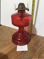 Full view of the red glass oil lamp approximately 11 inches tall with brass burner and wick on top.