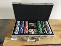 Open silver metal case showing organized poker chips in white, blue, red, green, black and accessories inside black interior.