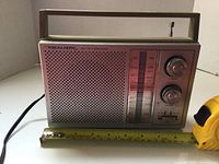 Left side view of Realistic portable radio, showing front speaker grille with pink and silver finish, frequency scale, and control knobs.