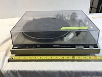 Front view of the Technics turntable with clear dust cover, ruler placed in front showing width approximately 16 inches.