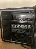 Interior photo showing three wire shelves including a bottle rack, black interior, and power cord at base.