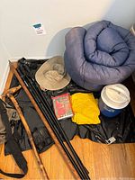 Overall lot photo showing rolled sleeping bag, walking sticks, hat, rain ponchos and cooler