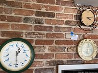Three vintage items displayed on brick wall: 13.5 inch bird clock, 10 inch temperature gauge, and 11.5 inch vintage lock