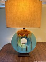 Front view of blue ceramic circular lamp base with beige drum shade lit.