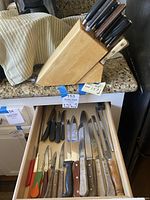 Overhead view of the open drawer with multiple knives showing various handle materials and blade types, next to the wooden knife block with knives inserted.