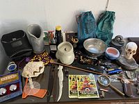 Overview of assorted collectibles including letter openers, skull ashtray, dragon jewelry box, vases, bank bags, candle, shell, exercise balls, metal bowl, beads, flashlight, pen holder, postcards and more on display.
