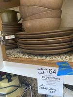 Stack of seven brown ceramic dinner plates with four matching bowls above