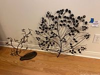 Full view of both metal tree wall hanging and jewelry tree with tray placed on floor against wall.