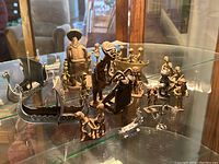 Wide view of all miniature metal sculptures displayed on glass shelf including Nordic boats and African figures.