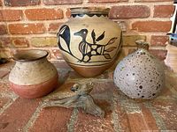 Front view of the four items including the large Native American vase with bird design, two smaller pottery vases, and the small bird sculpture on driftwood.