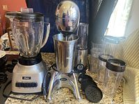 Photo showing Oster traditional blender with glass jar and multiple Bella Cucina plastic cups and lids on countertop.