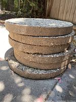 Stacked view of six round concrete stepping stones showing thickness and rough aggregate texture on edges.