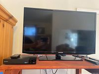 Samsung 32 inch UN32EH5000F TV with remote on the right and Sony Blu-ray DVD player with remote on the left, placed on wood surface.