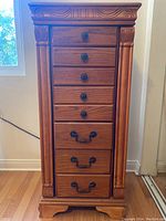 Front view of tall wooden jewelry cabinet with 8 drawers and decorative carved details