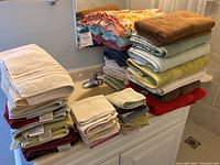 Large assortment of assorted bathhouse towels neatly stacked on a counter, including hand, face, and bath towels in multiple colors.