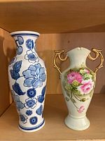 Blue and white Chinese-style vase alongside fine china floral vase with gold handles on wooden shelf