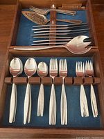 Wooden box with blue felt lining holding multiple flatware pieces: knives, servers, spoons and forks